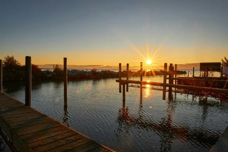 Sunrise bursting between weathered dock pilings, its light scattering in gold streaks across still marina water.